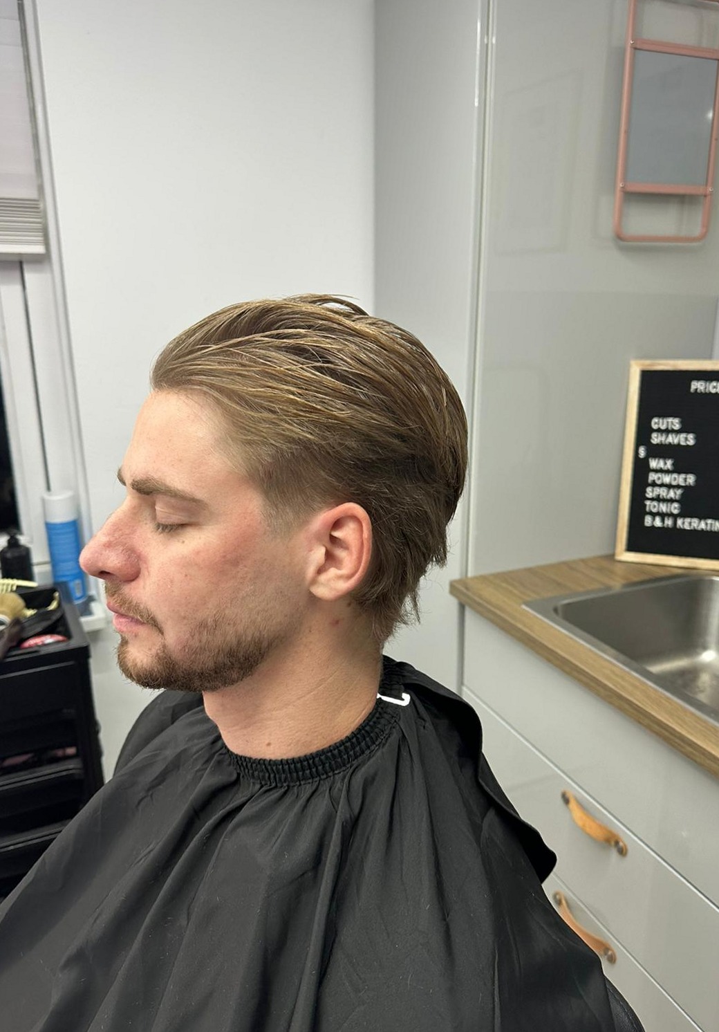 Klant in de kapmantel, van opzij, met een vers geknipt en gestyled kapsel